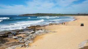 Uma praia com ondas, rochas e um sistema de dunas.
