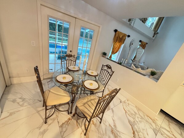A dining area with a round glass table, six chairs, and a view of a snowy landscape through large windows.