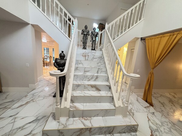 Un escalier en marbre, avec des rampes blanches et un rideau doré sur la droite.