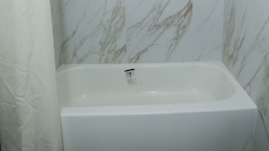 Un baño con ducha, bañera y paredes de mármol.
