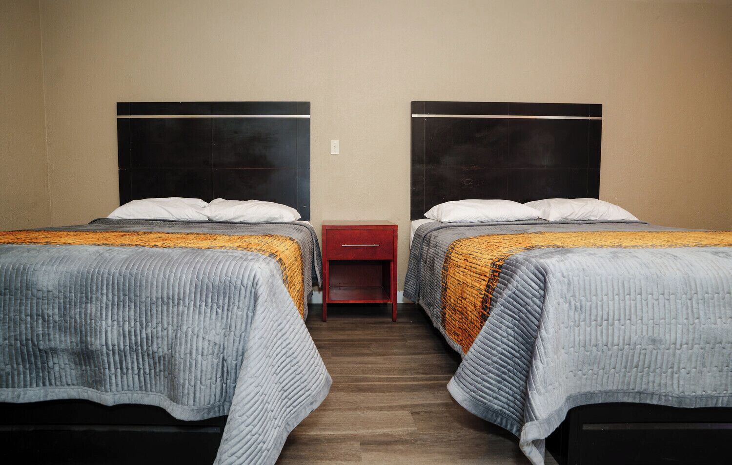 A hotel room with two beds, each with a headboard, a nightstand, and a drawer.