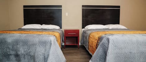 A hotel room with two beds, each with a headboard, a nightstand, and a drawer.