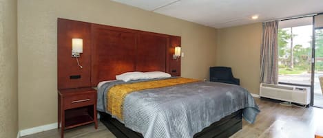 A hotel room with a bed, bedside tables, a chair, a window with curtains, and an air conditioning unit.