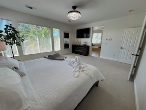 Un dormitorio con una cama grande, un televisor, un aparador y una puerta que da a otra habitación.