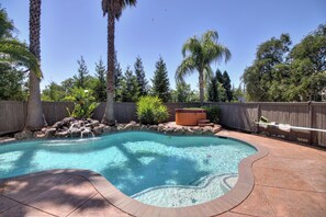A backyard with a swimming pool, surrounded by a wooden fence, palm trees, and a hot tub.