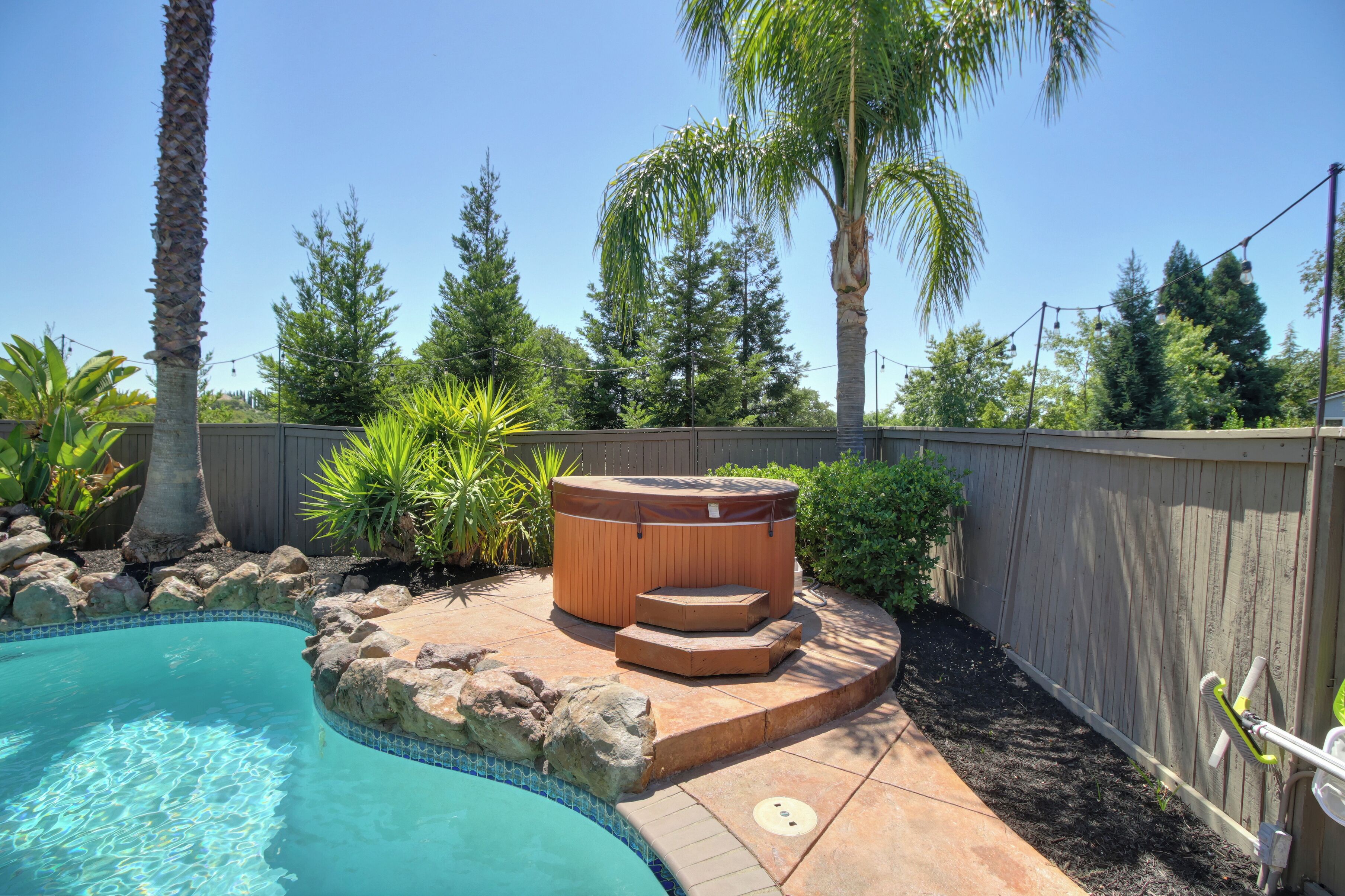 Ein Garten mit Schwimmbad, Whirlpool und einer Holzterrasse.