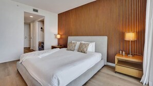 A modern hotel room with a large bed, wooden panel wall, and a nightstand with a lamp. - New! Canal View Studio - Resort Perks Beach (Hallandale Beach)