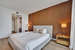 A modern hotel room with a large bed, wooden panel wall, and a nightstand with a lamp. - New! Canal View Studio - Resort Perks Beach (Hallandale Beach)
