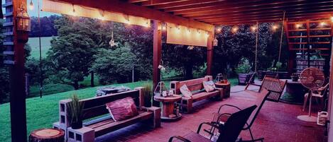 Un patio al aire libre con una pérgola de madera, zona de estar y luces colgantes.
