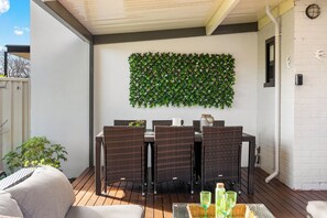 A patio area with a table and chairs, a decorative wall, and a white brick wall. - Glandore Charm Contemporary Haven near CBD and Coast (Glandore)