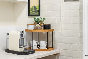 A kitchen counter with a coffee machine, a shelf with a plant, and a framed picture on the wall. - Glandore Charm Contemporary Haven near CBD and Coast (Glandore)