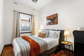 A hotel room with a bed, a bedside table with a lamp, a wall-mounted artwork, and a window with blinds. - Glandore Charm Contemporary Haven near CBD and Coast (Glandore)
