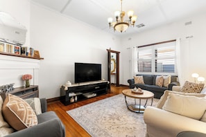 A living room with a television, sofa, and a chandelier. - Glandore Charm Contemporary Haven near CBD and Coast (Glandore)