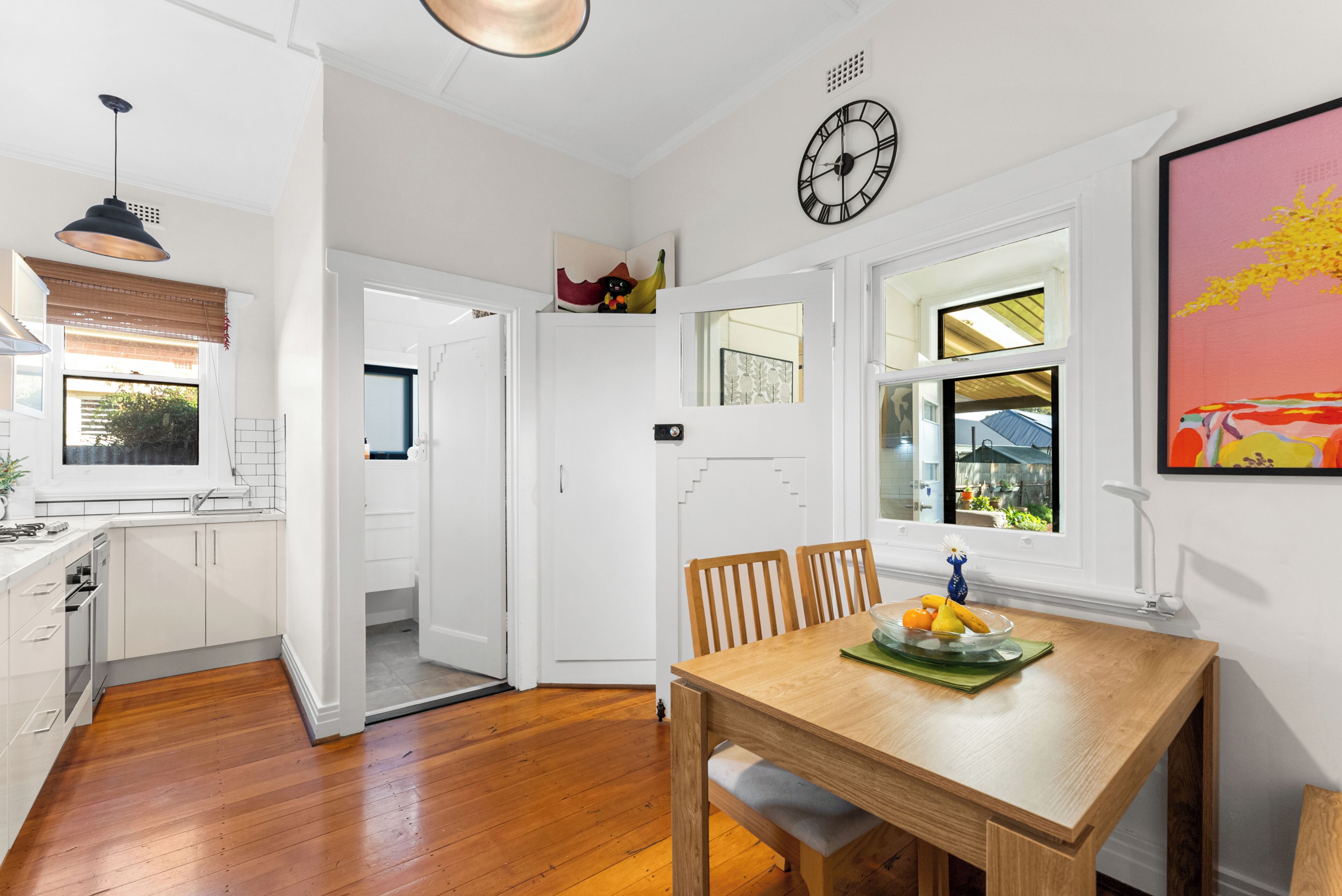 A modern kitchen with white cabinetry, a wooden dining table with chairs, and a clock on the wall.