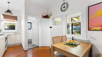 A modern kitchen with white cabinetry, a wooden dining table with chairs, and a clock on the wall.