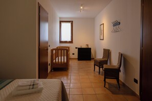 Un dormitorio con cama, cuna de madera, silla, cómoda y ventana con cortinas.