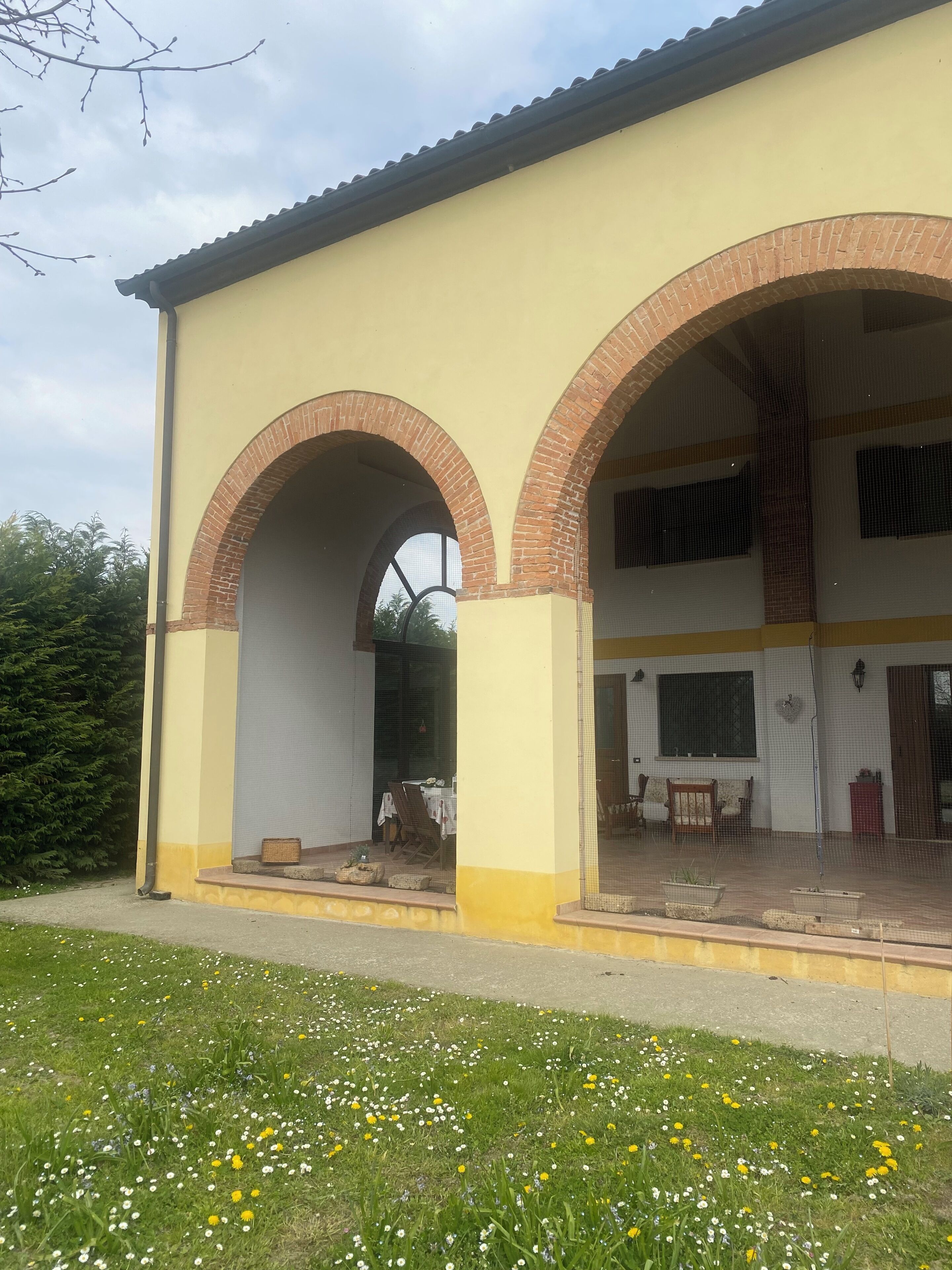 Un edificio con facciata gialla, due archi in mattoni e una veranda coperta con mobili da esterno.