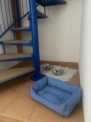 A blue staircase with a pet bed and two metal bowls on a tiled floor.