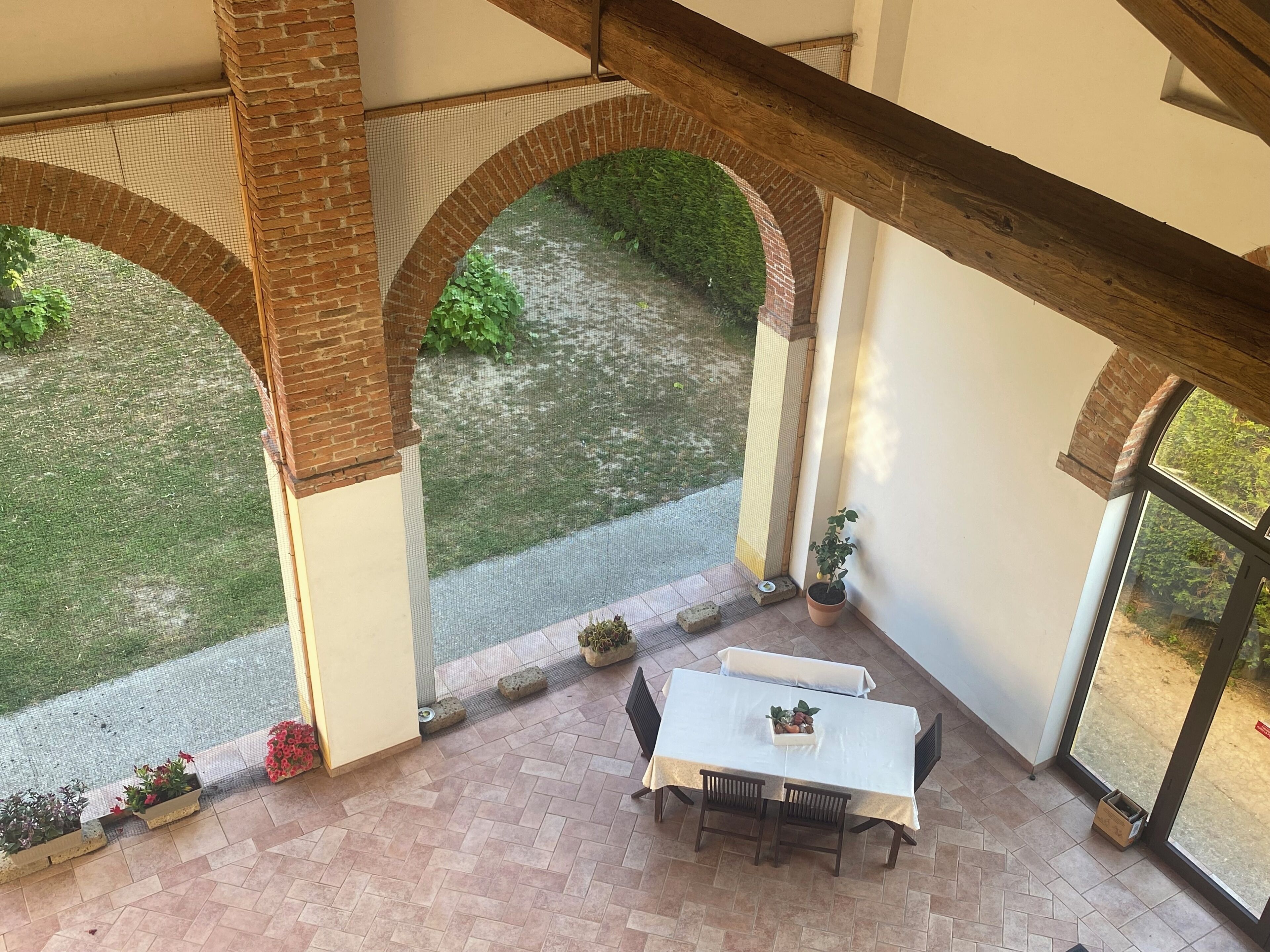 Un porche cubierto con mesa y sillas, arcos de ladrillo y vistas al jardín.