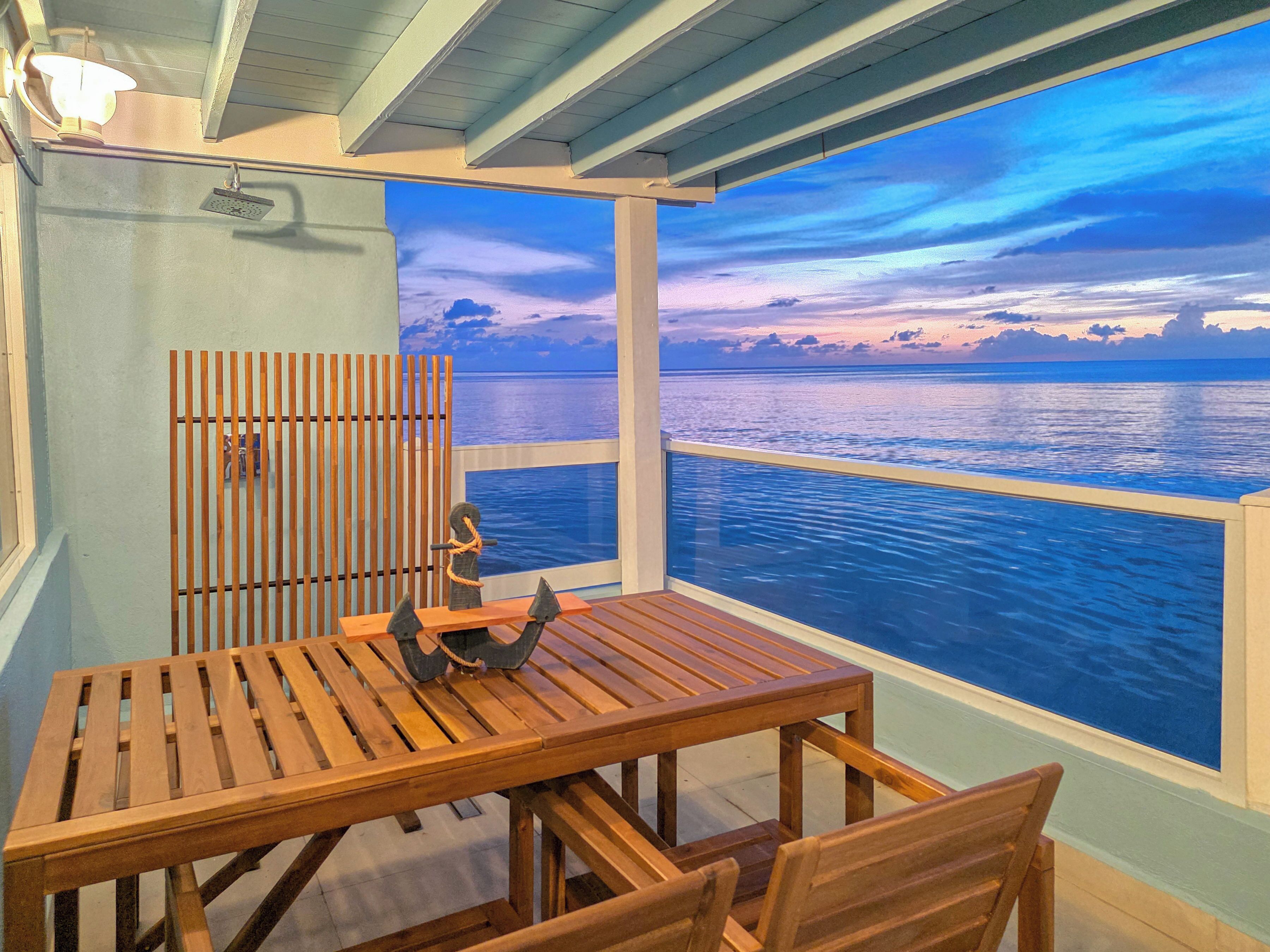 A wooden table and chairs in a room with a view of the ocean.