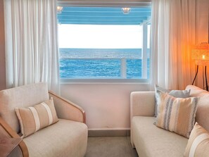 A room with a view of the sea through a window, two sofas, and a floor lamp.