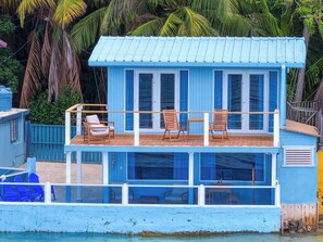 A blue houseboat with a deck, two chairs, and a table.