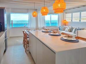 A modern kitchen with a central island, dining area, and a view of the sea.