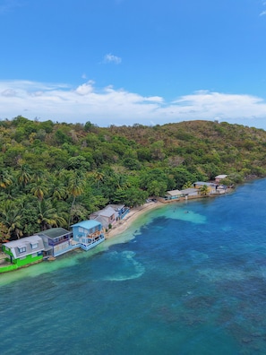 Una zona costiera con spiaggia, acque blu cristalline e una collina ricoperta di bosco.