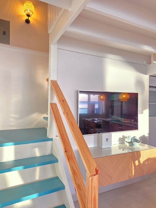 A staircase with blue steps and a wooden handrail, leading to a room with a flat-screen TV mounted on the wall.