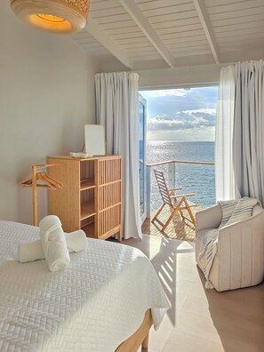 A room with two beds, a wooden cabinet, a chair, and a view of the sea.