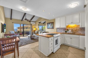 A spacious kitchen with white cabinets, a large island, and a view to the outside. - Shores of Maui 208 - Ocean Front! Across from Beach & Central Location (Kihei)
