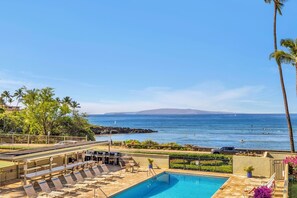 A pool area with lounge chairs and a view of the ocean. - Shores of Maui 208 - Ocean Front! Across from Beach & Central Location (Kihei)