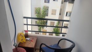 Een balkon met een stoel, een tafel, een rode gasfles en een gele slang.