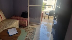 Een kamer met een bed, een klein tafeltje met een document, een stoel en een glazen schuifdeur die leidt naar een buitenbalkon.