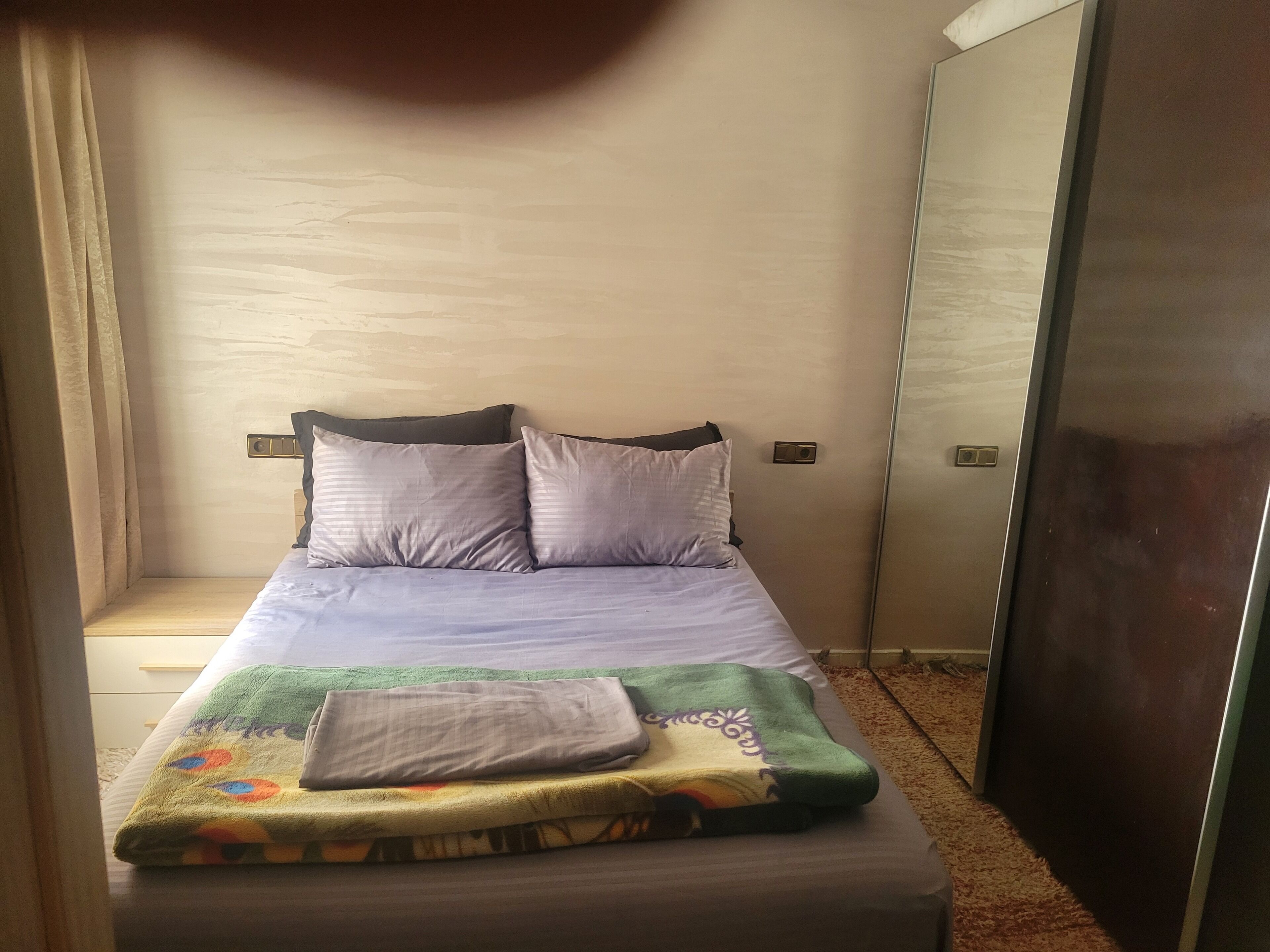 Ein Einzelbett mit grauer Decke und Kissen, ein Nachttisch und ein Kleiderschrank.