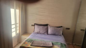 Una cama individual con cabecera, una ventana con persianas y un espejo en la pared.
