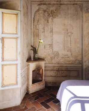 A room with a bed, a small table with a vase and a flower, and a wall with a decorative panel. - Borgo Santa Croce Design Florence Luxury Management (Firenze)
