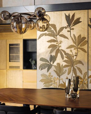 A dining area with a wooden table, chairs, a wall-mounted light fixture, and a decorative wall panel. - Borgo Santa Croce Design Florence Luxury Management (Firenze)