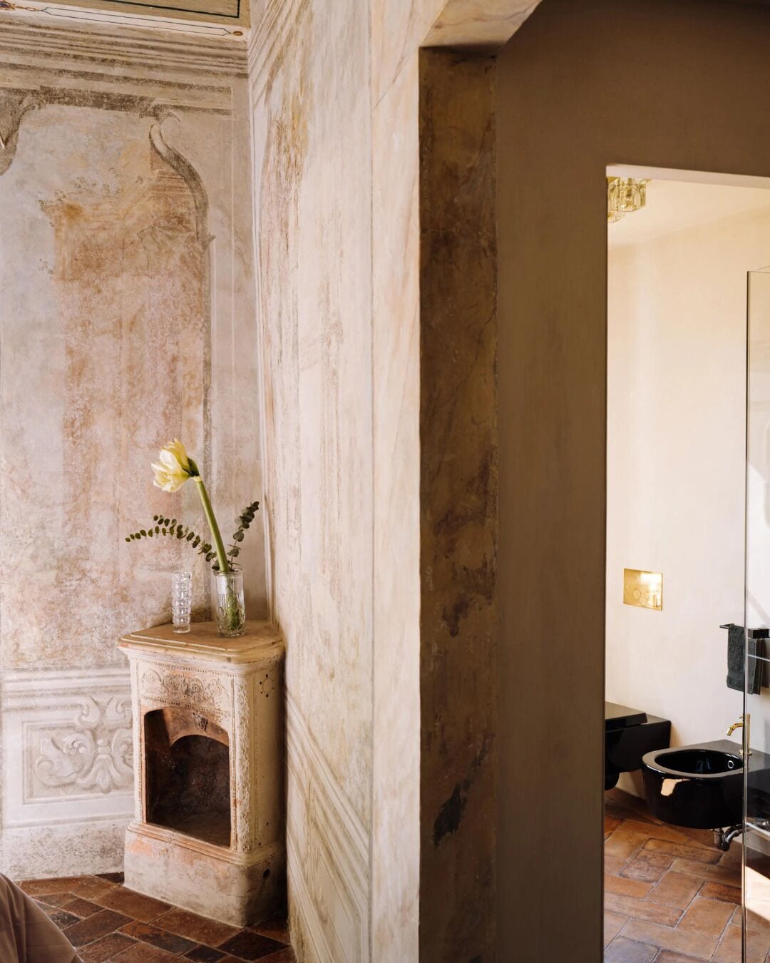A room with a fireplace, a vase with flowers, and a modern bathroom visible through an open door.