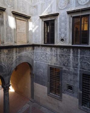 A courtyard with a stone wall, multiple windows, and an arched entrance. - Borgo Santa Croce Design Florence Luxury Management (Firenze)