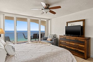 A bedroom with a bed, a dresser, a television, and a balcony with a view of the ocean. - Birds Eye View Condo (Panama City Beach)