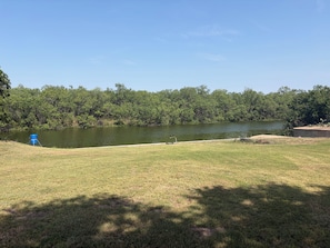A grassy area with a body of water, trees, and a blue container.