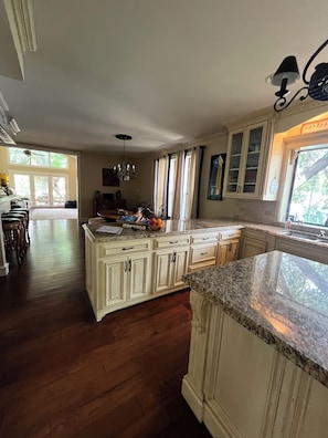 A spacious kitchen with a large island, wooden cabinets, and a view of the outdoors through a window.