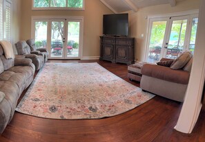 A living room with a large sectional sofa, a patterned rug, a television, and a cabinet.