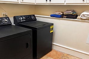 A laundry area with two black washing machines and a shelf with folded clothes.