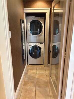 A laundry room with two stacked front-loading washing machines and a door leading to another room.