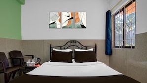 A hotel room with a bed, a coffee table with cups and a kettle, a window with curtains, and abstract art on the wall. - Saver Double Crystal Holiday Homes (Calangute)