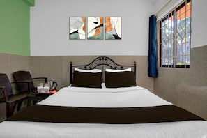 A hotel room with a bed, a coffee table with cups and a kettle, a window with curtains, and abstract art on the wall. - Saver Double Crystal Holiday Homes (Calangute)