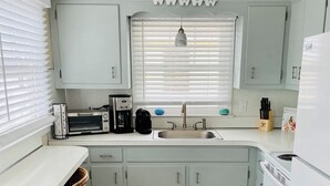 A kitchen with white cabinets, a white countertop, a sink, a stove, and two wicker chairs.