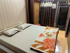 Una cama individual con edredón floral, un armario de madera y una cortina estampada.